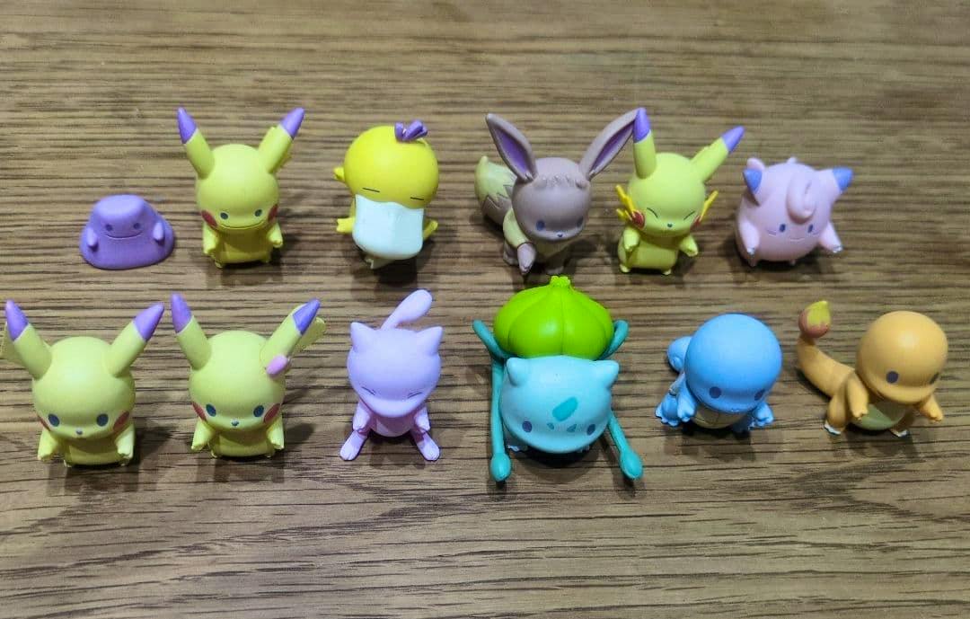 Twelve small plastic Pokémon figures from the advertised full 12-piece set arranged on a wooden surface in two rows.
