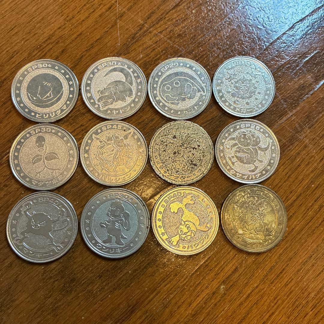 Twelve Pokémon metal medal coins arranged in rows on a wooden surface.