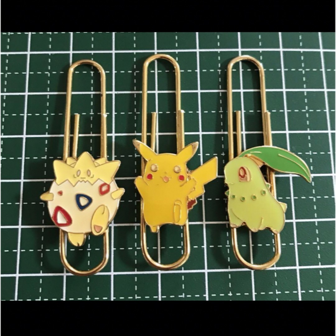 Three metal Pokémon paper clips with character charms shown front-side on a green grid background.