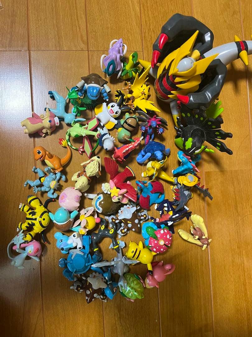 Many small plastic Moncolle figures scattered on a wooden floor.