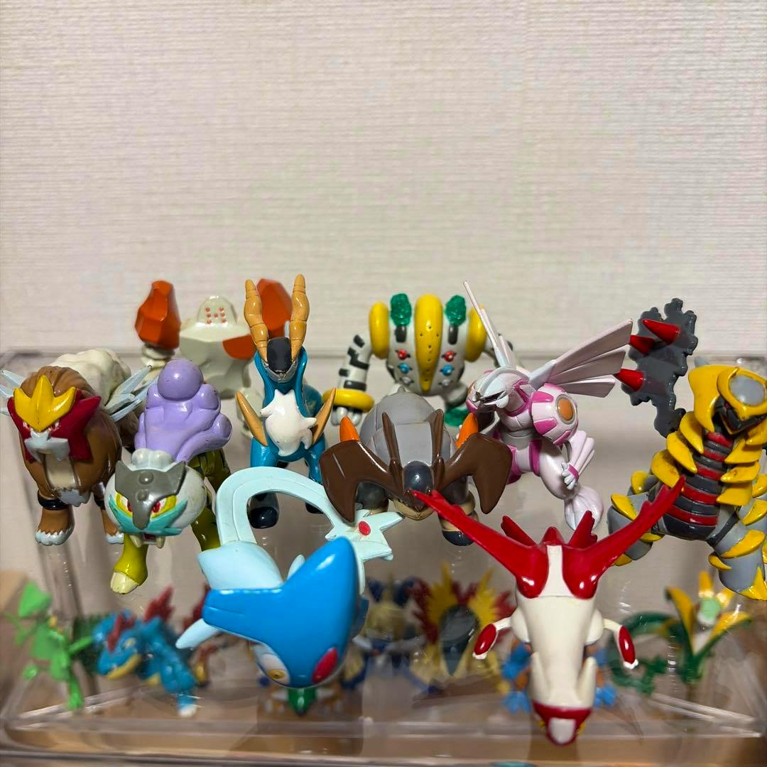 Multiple small plastic Pokémon Moncolle figures (legendary and semi-legendary) shown from the front on a clear display stand.