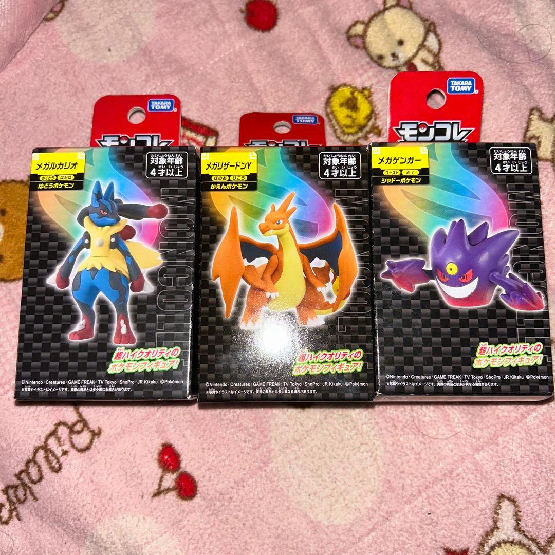 Three boxed MonColle figure packages showing Mega Lucario, Mega Charizard Y, and Mega Gengar arranged side by side on a blanket.