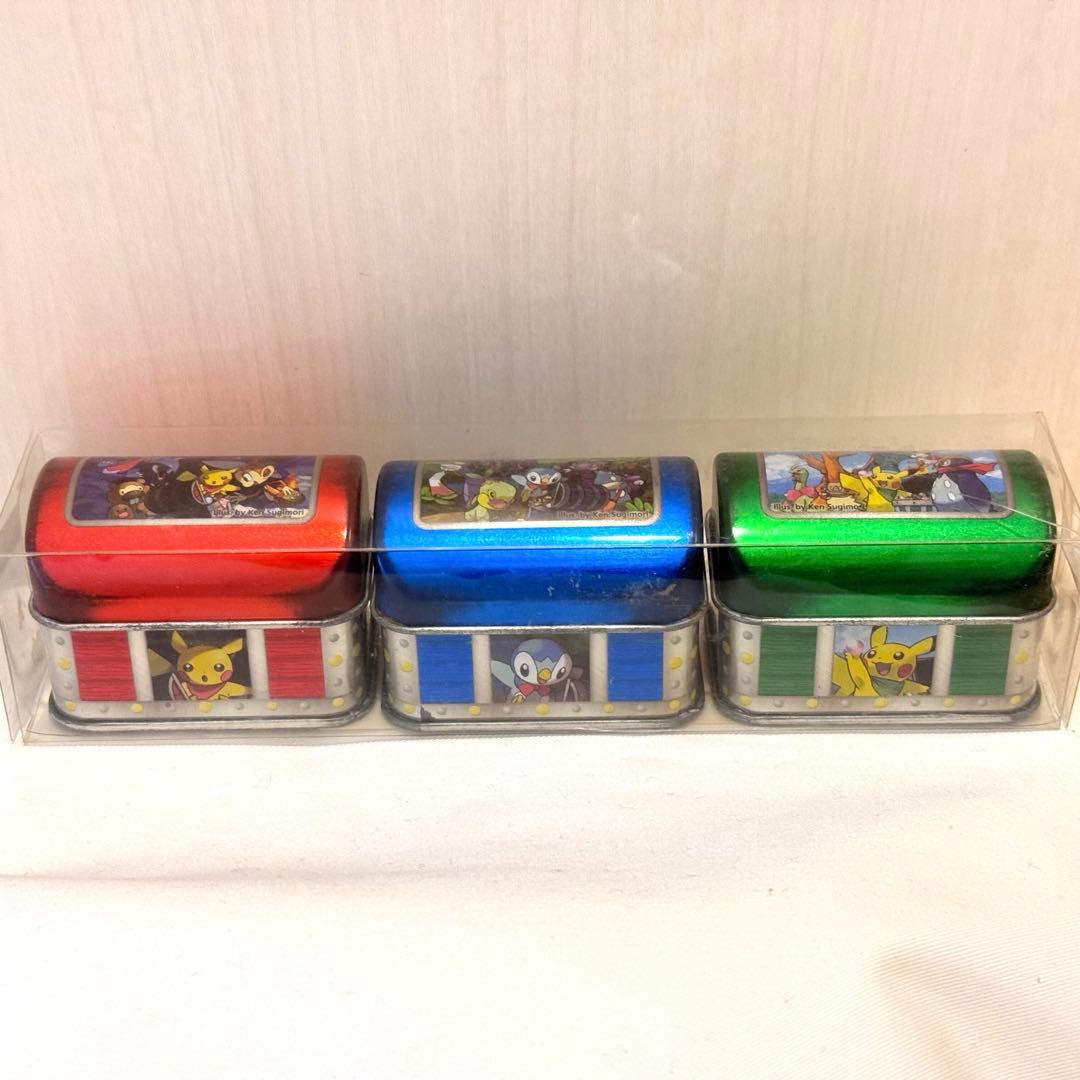 Three Pokémon-themed metal candy tins displayed in a clear plastic case, front view.