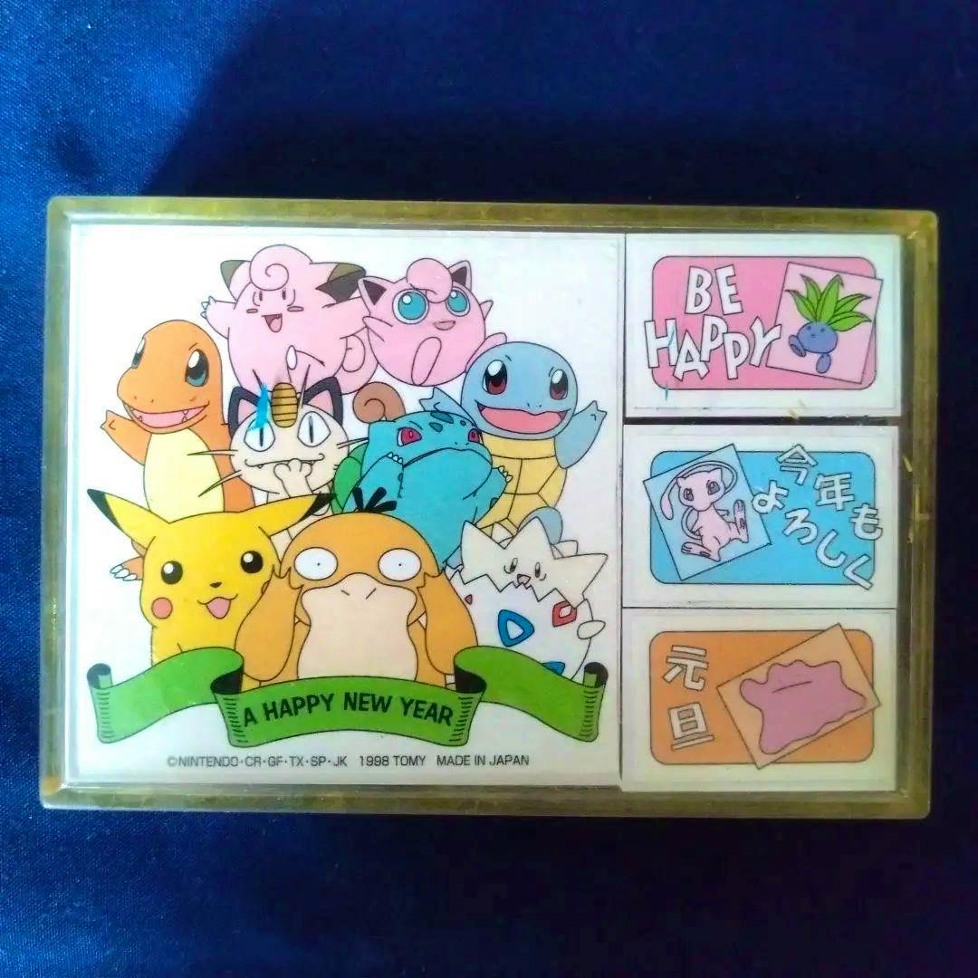 Front view of the Pokémon New Year wooden stamp set in its case showing printed Pokémon artwork and three small rectangular stamp designs with a banner reading "A HAPPY NEW YEAR".