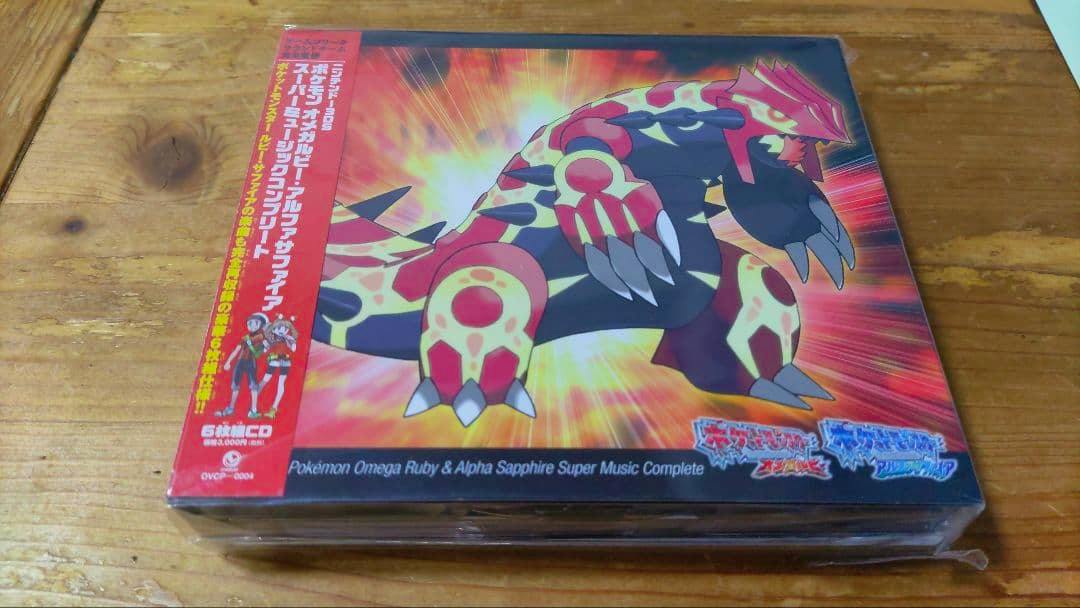 Front of the CD set for 3DS Pokémon Omega Ruby & Alpha Sapphire Super Music Complete showing Groudon artwork on a wooden table.