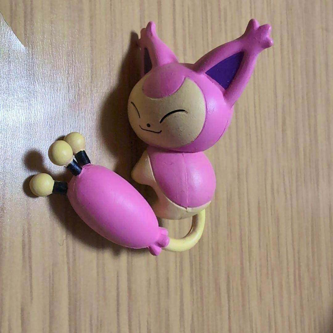 Plastic Pokémon figure てのひらモーメント ニャオハ (Nyaho) lying on a wooden surface, showing pink and cream colors.