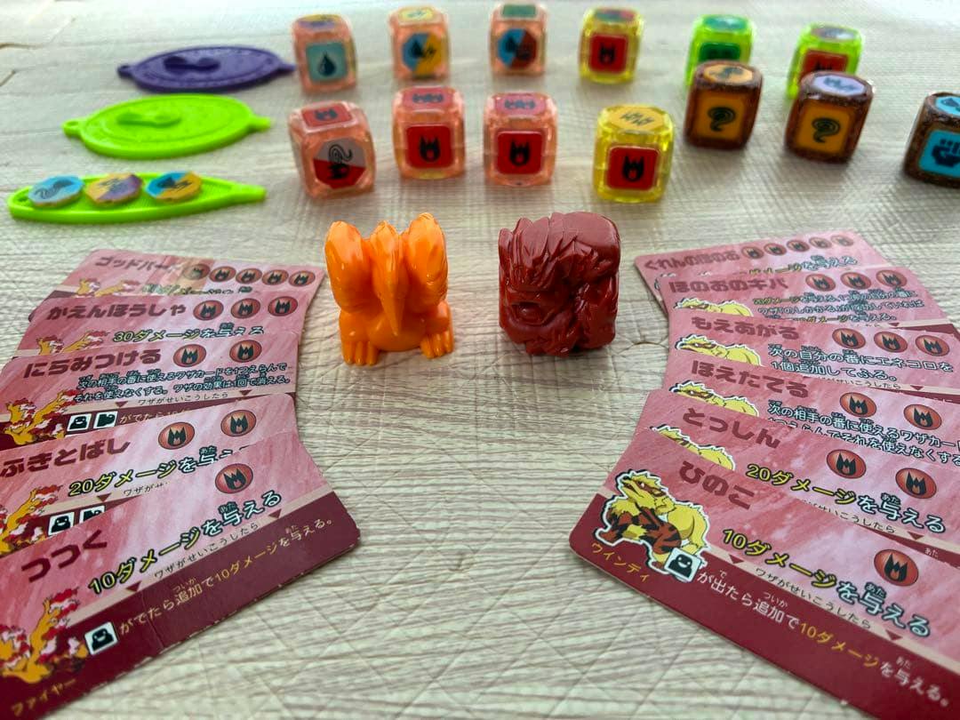 Two small plastic Pokémon figure pieces centered amid game cards, translucent dice, and tokens on a textured surface.