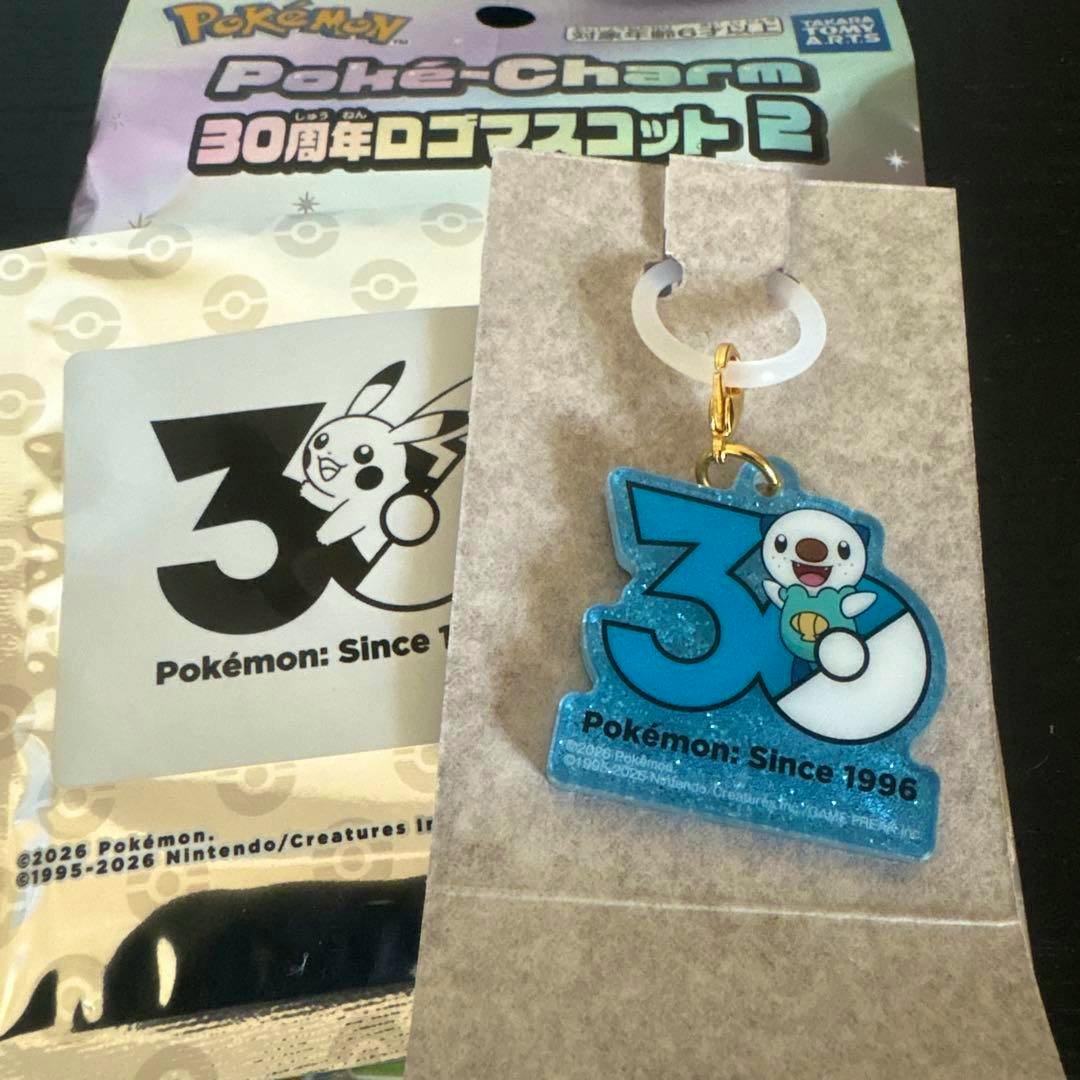 A blue glitter acrylic 30th-anniversary Pokémon keychain featuring Mijumaru (Oshawott) with a gold clasp displayed on its backing card.