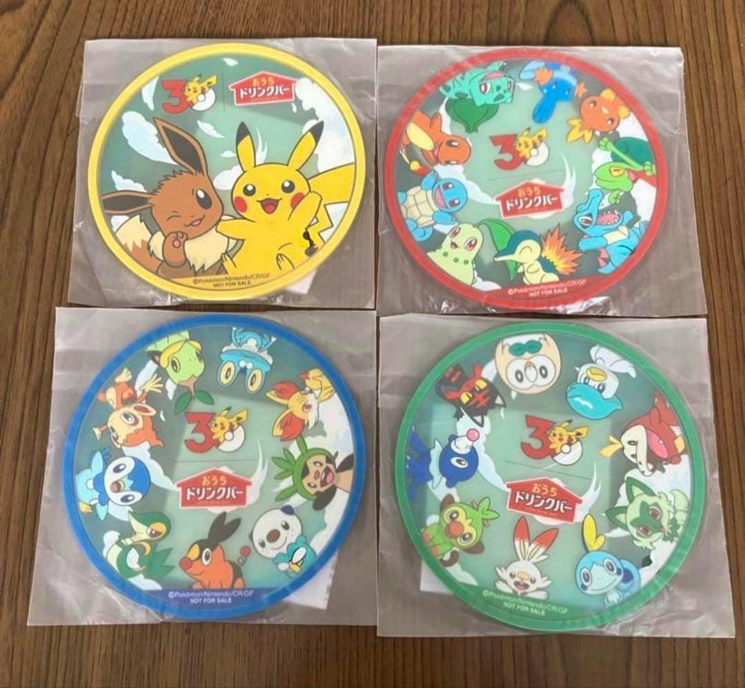 Four round Pokémon coasters in individual plastic sleeves arranged in a 2x2 grid on a wooden surface.