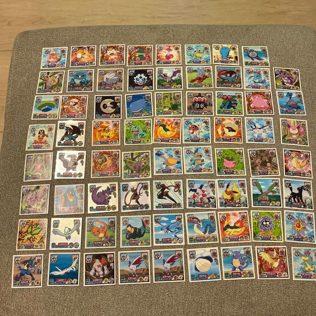 A large assortment of square Pokémon stickers from a bulk set arranged in rows on a carpeted surface.
