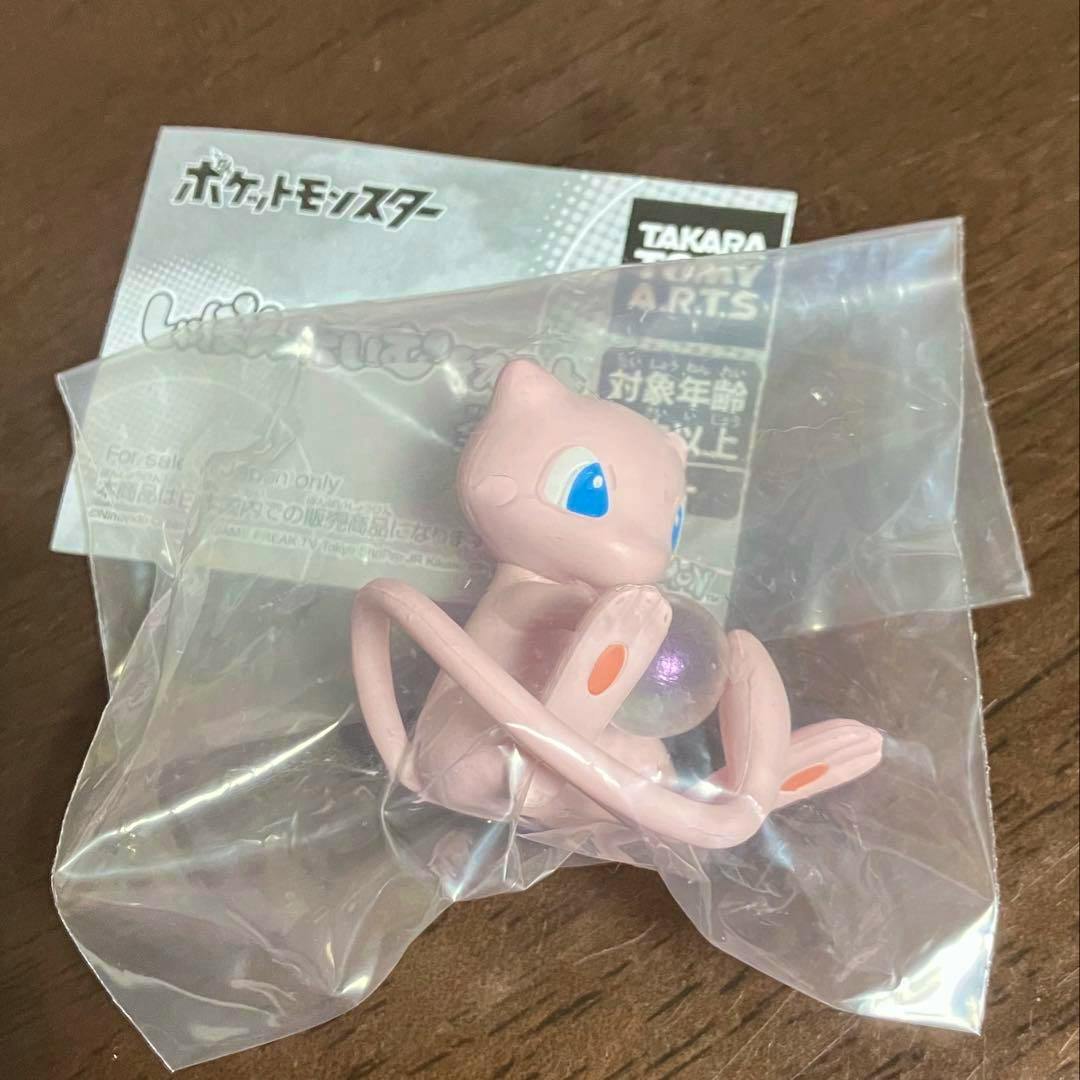 Pink Mew plastic figure holding a clear bubble, pictured inside a clear plastic bag on a wooden surface with its paper insert behind it.
