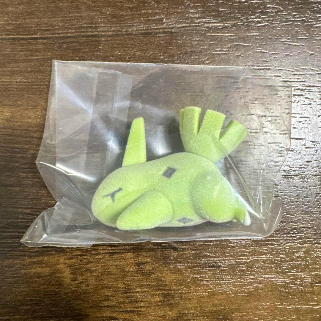 A green Pokémon Sleep figure (ヨーギラス / Larvitar) sealed in a clear plastic bag resting on a wooden surface.