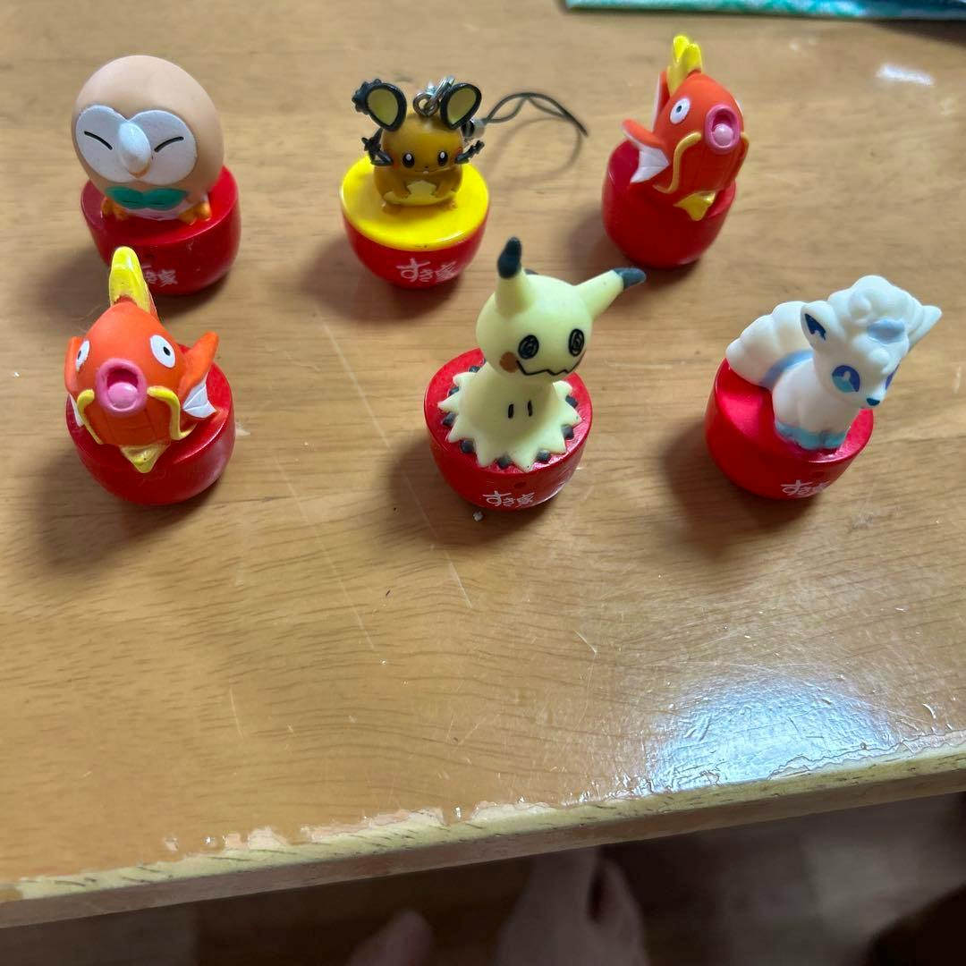 Six Pokémon plastic figures on red Sukiya bases arranged on a wooden table.