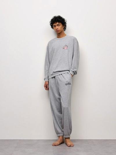 Male model wearing a grey long-sleeve sweatshirt and matching long pants Pokémon lounge set, standing against a plain light wall.
