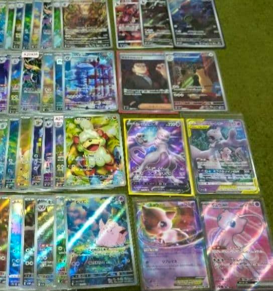 Multiple Pokémon trading cards, including Mew and Mewtwo tag team GX holo cards, laid out on a green surface.
