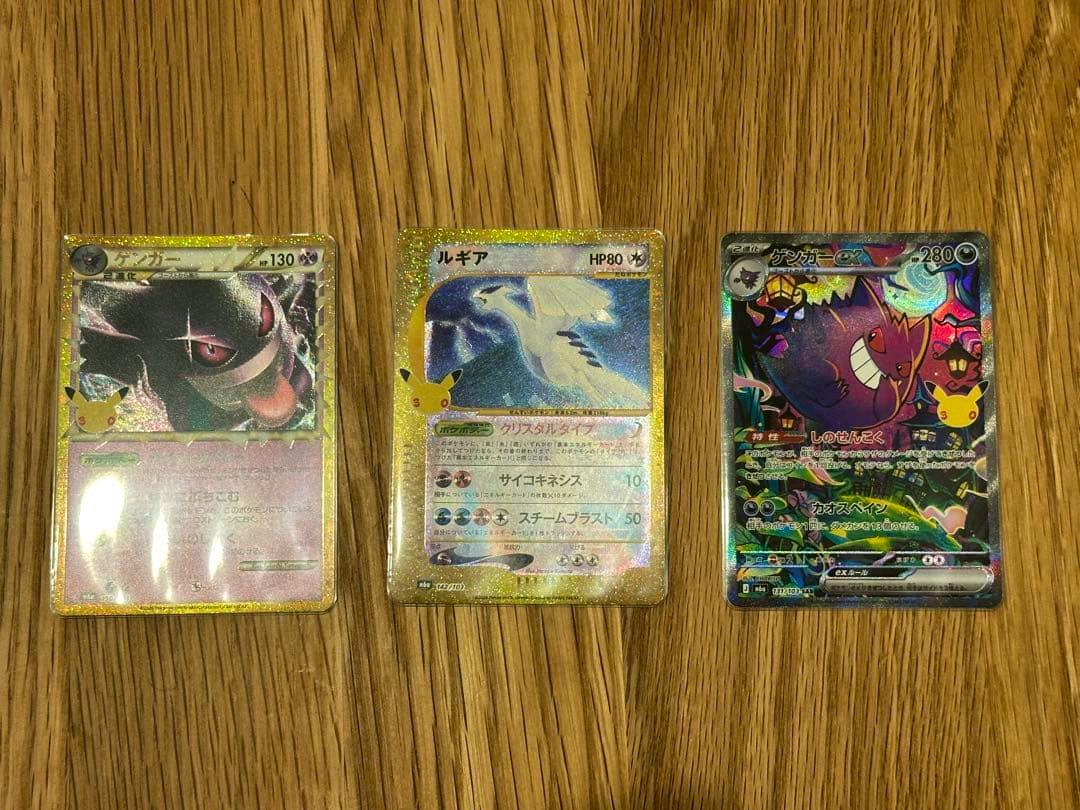 Three Pokémon trading cards (Lugia and two Gengar) shown front-side on a wooden surface.