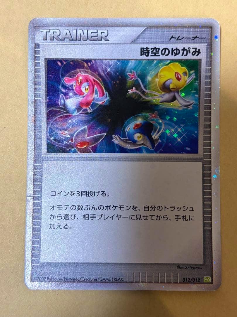 Photograph of the front of the trading card "時空のゆがみ" (012/012 PtS) showing the Trainer artwork and Japanese text on a beige background.