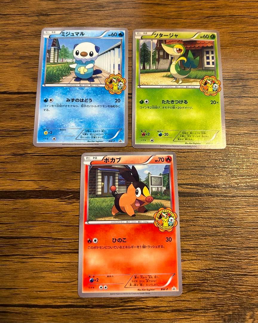 Three Pokémon trading cards showing their front artwork laid out on a wooden surface.