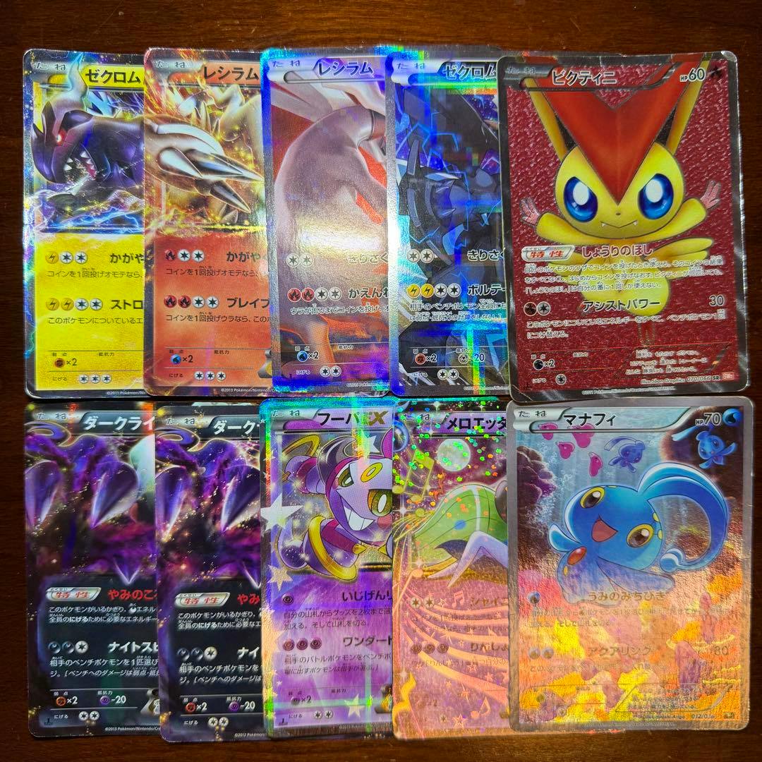 A top-down photo of multiple Japanese Pokémon trading cards showing holographic fronts, including a Victini SR card.