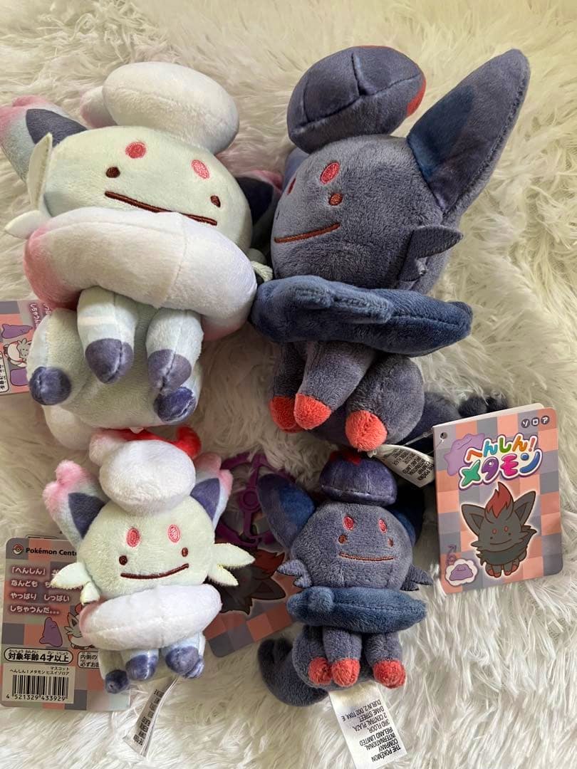 Four Zorua and Hisuian Zorua plush mascot toys arranged on a fluffy surface with tags visible.