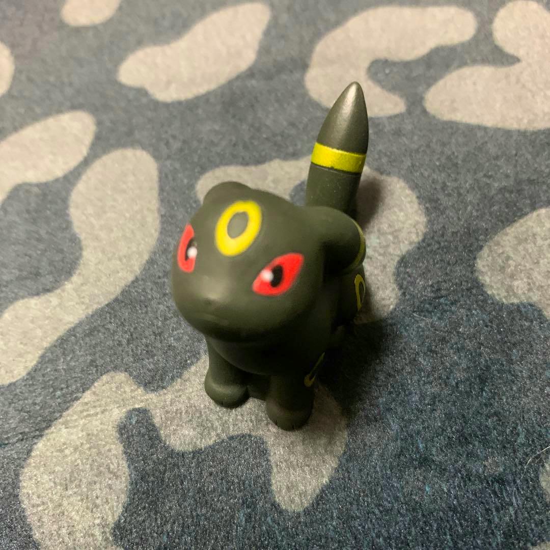 Front three-quarter view of a plastic Umbreon (ブラッキー) Pokémon figure placed on patterned fabric.