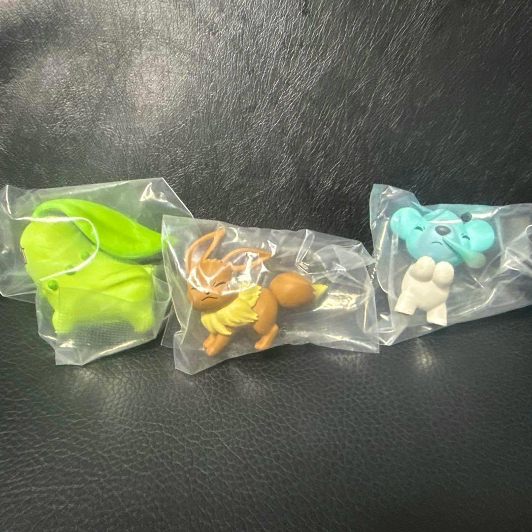 Three small Pokémon plastic figures (Chikorita, Eevee, and Cubchoo) individually bagged and displayed on a black surface.