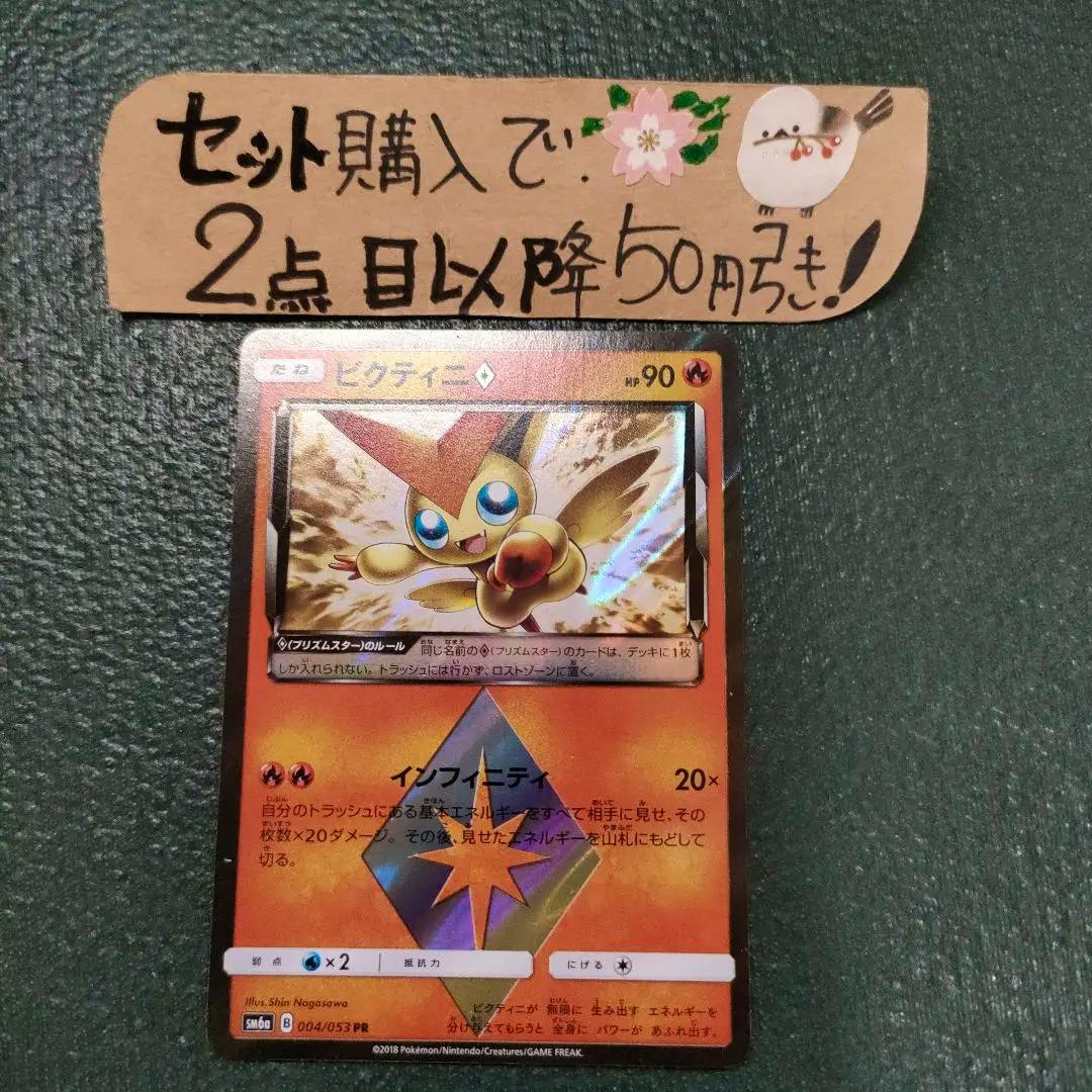 Photo of the Pokémon Victini Prism Star Infinity trading card on a green surface with a handwritten promotional note above.
