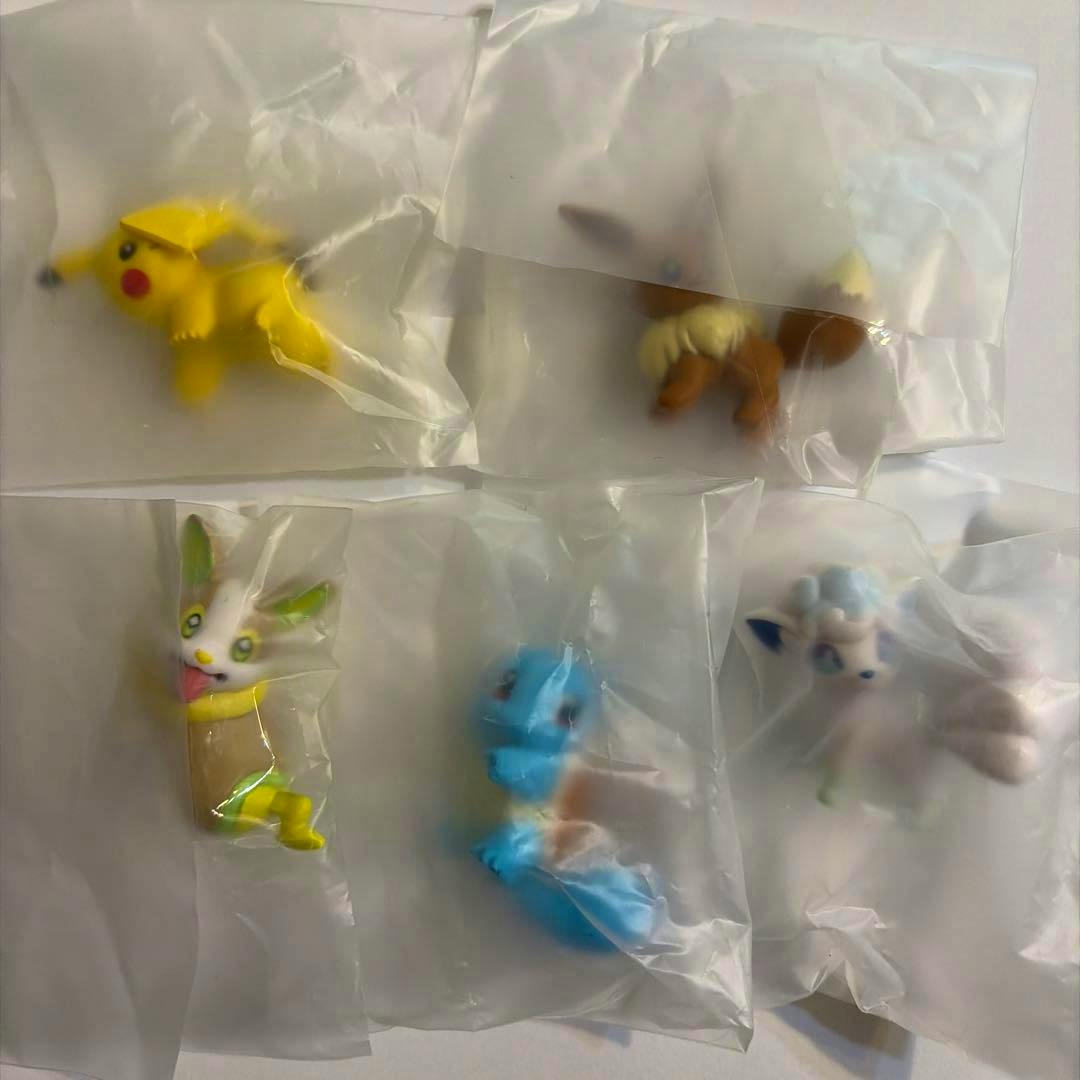 Five Pokémon gacha capsule figures (Pikachu, Eevee, Squirtle, Alolan Vulpix, and Yamper) sealed individually in clear plastic bags on a white background.