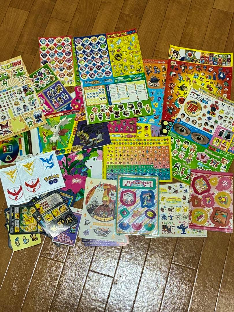 Multiple sheets of stickers, including Pokémon and Yo-kai Watch designs, spread out on a wooden floor.
