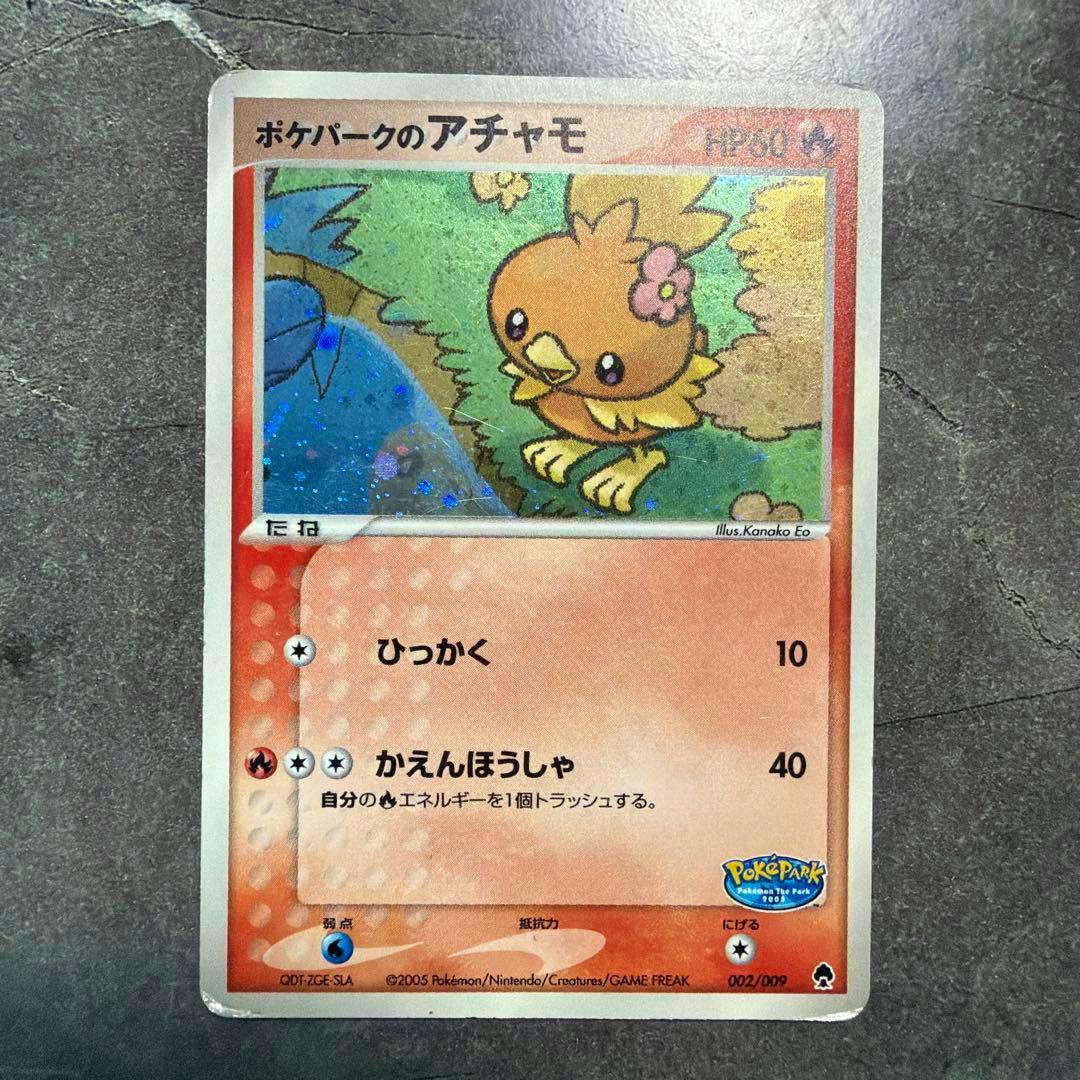 Photograph of the front of the Japanese ポケパークのアチャモ trading card showing the full holographic card on a dark textured surface.