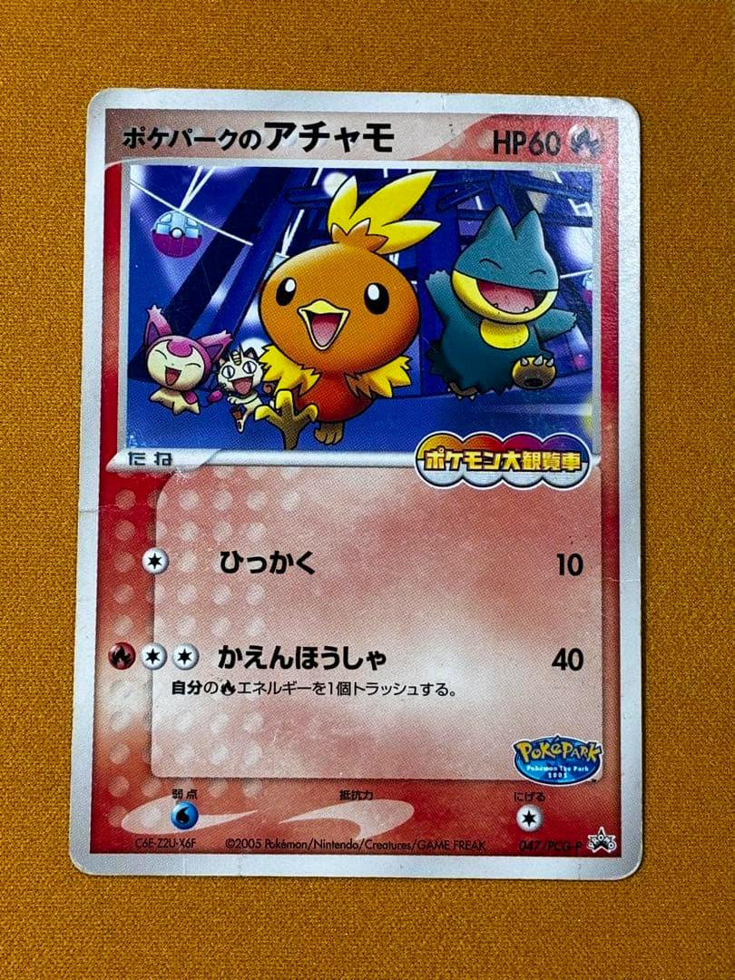 Front-view photo of the ポケパークのアチャモ promo trading card (047/PCG-P) placed on an orange fabric background, showing the card artwork and Japanese text.
