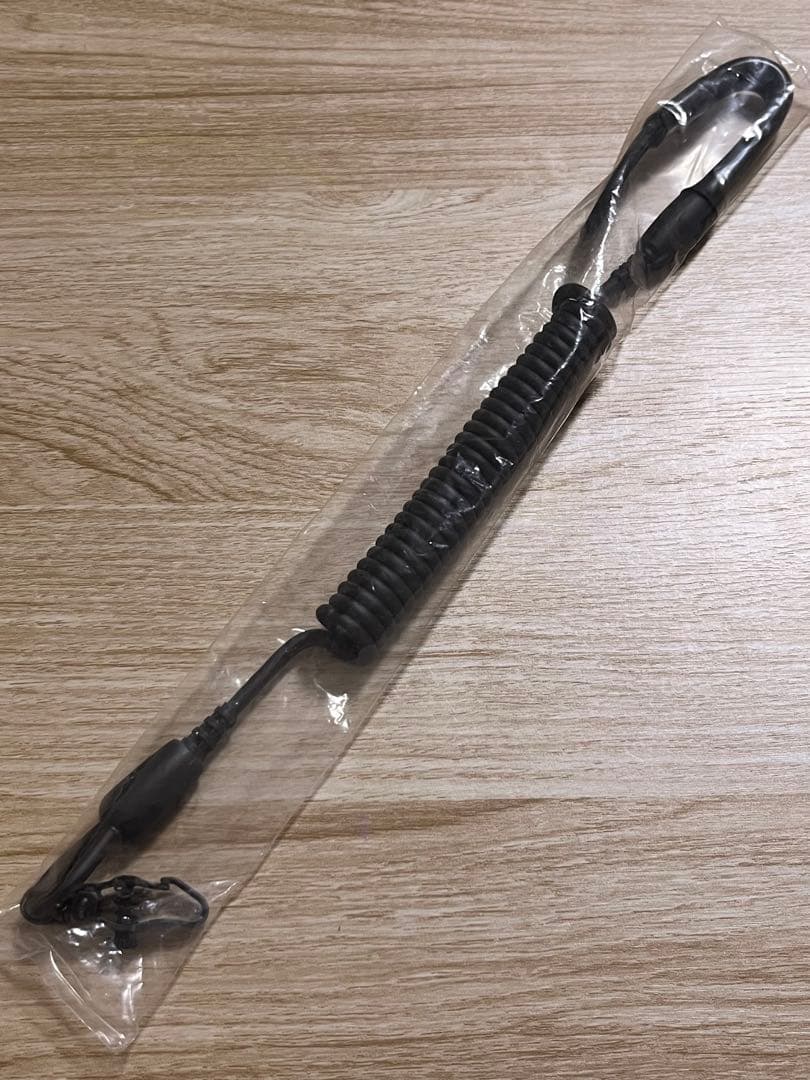Coiled black bungee cord with hooks packaged in clear plastic on a wooden surface.