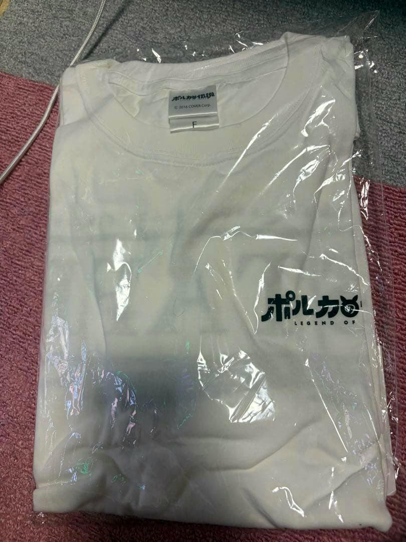 Folded white staff T-shirt (ポルカの伝説) in plastic packaging showing a small printed logo near the lower front and a visible neck tag.