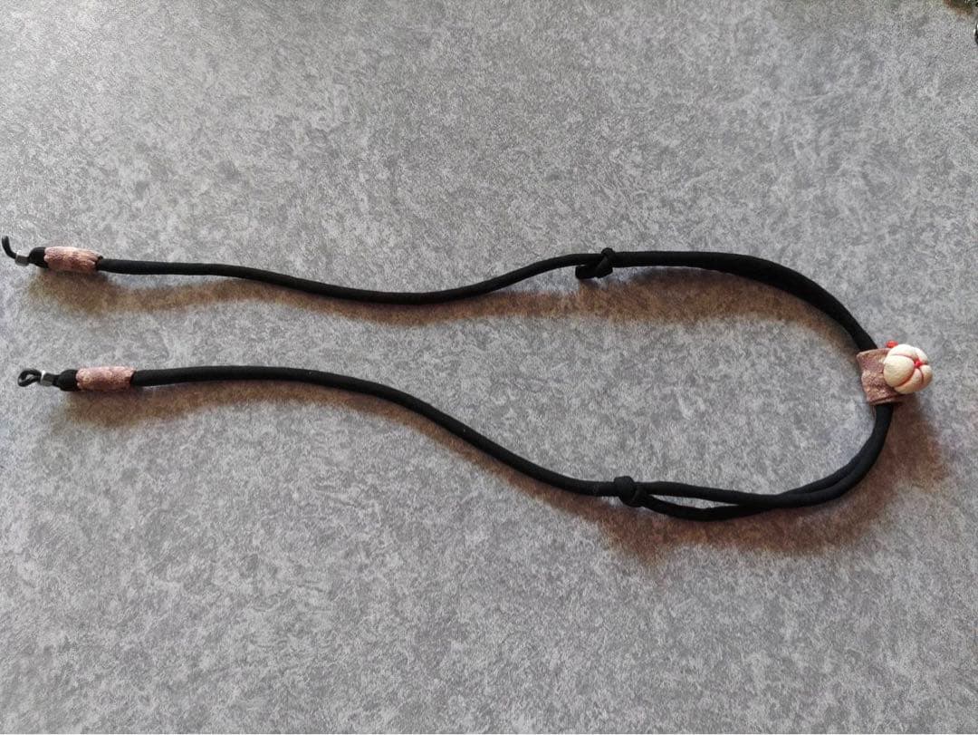 A black polyester eyeglass strap with decorative fabric bead and adjustable knots laid on a gray surface.