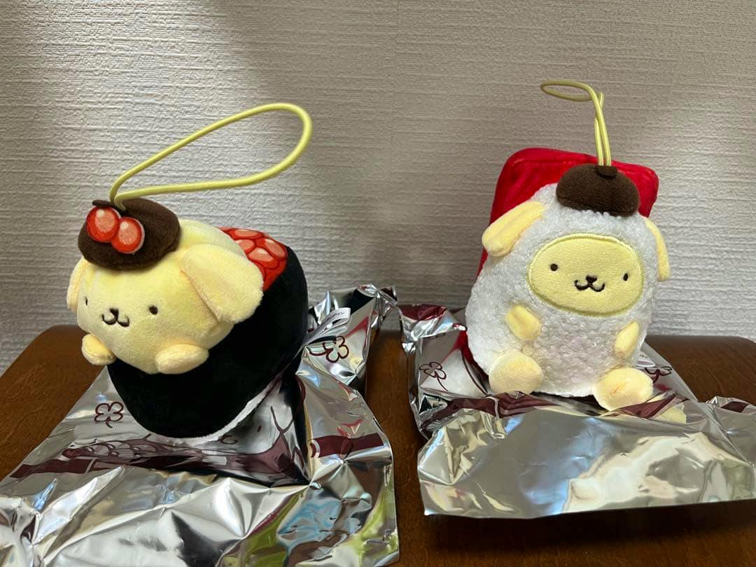 Two PomPomPurin plush keychains with hanging loops displayed side by side on a table.