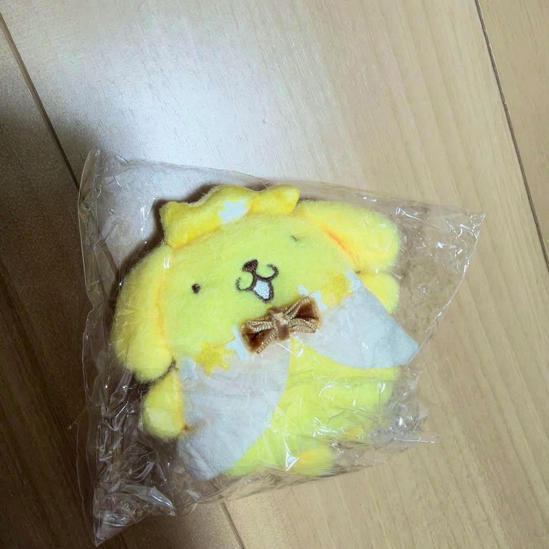 A yellow Pompompurin plush keychain wrapped in clear plastic and placed on a wooden floor.