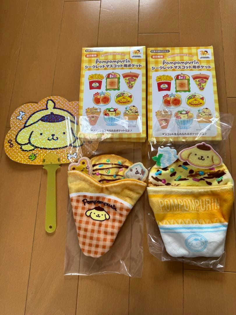 Two Pompompurin pockets for secret mascots with their packaging displayed on a wooden floor.
