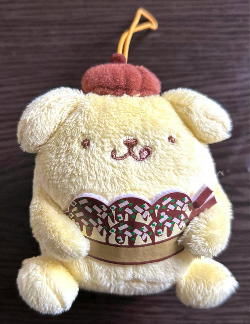 Front view of a yellow Pompompurin plush mascot with a brown beret and a takoyaki decoration on its belly.
