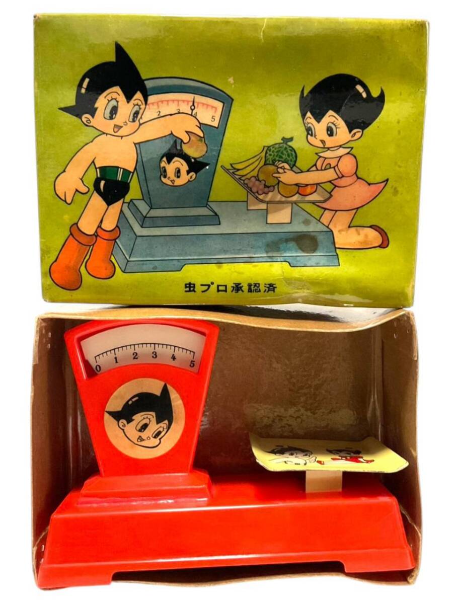 Red plastic toy scale with an Astro Boy illustration displayed inside its original cardboard box showing Astro Boy and Uran artwork.