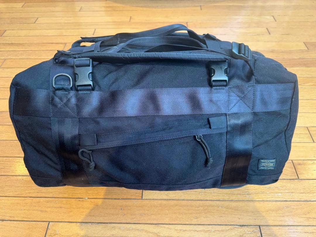 Black Porter 3WAY duffle bag on a wooden floor showing the front zip pocket, straps, and Porter logo patch.