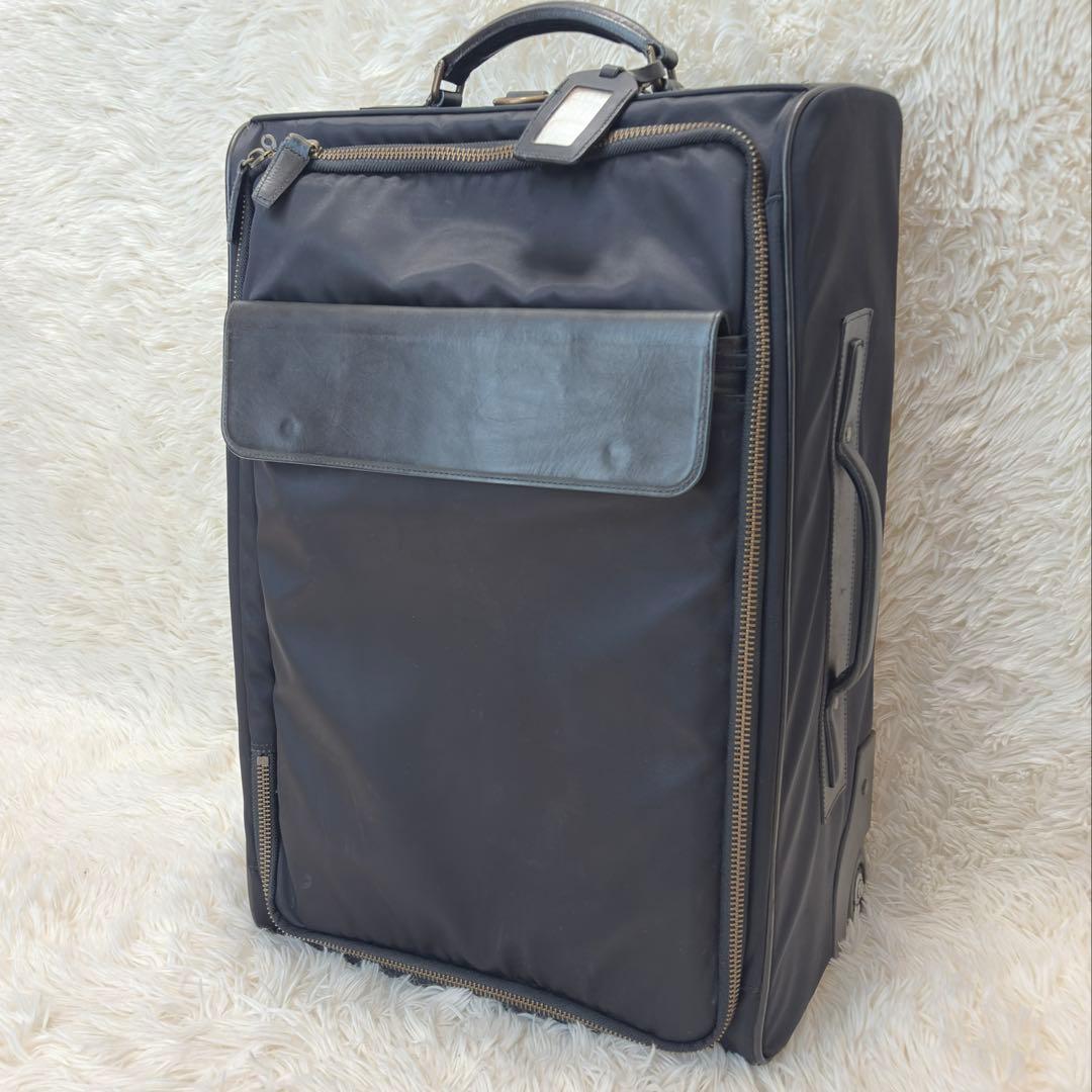 Angled front view of a black Porter cow-leather carry suitcase with handle and front pocket on a light rug.