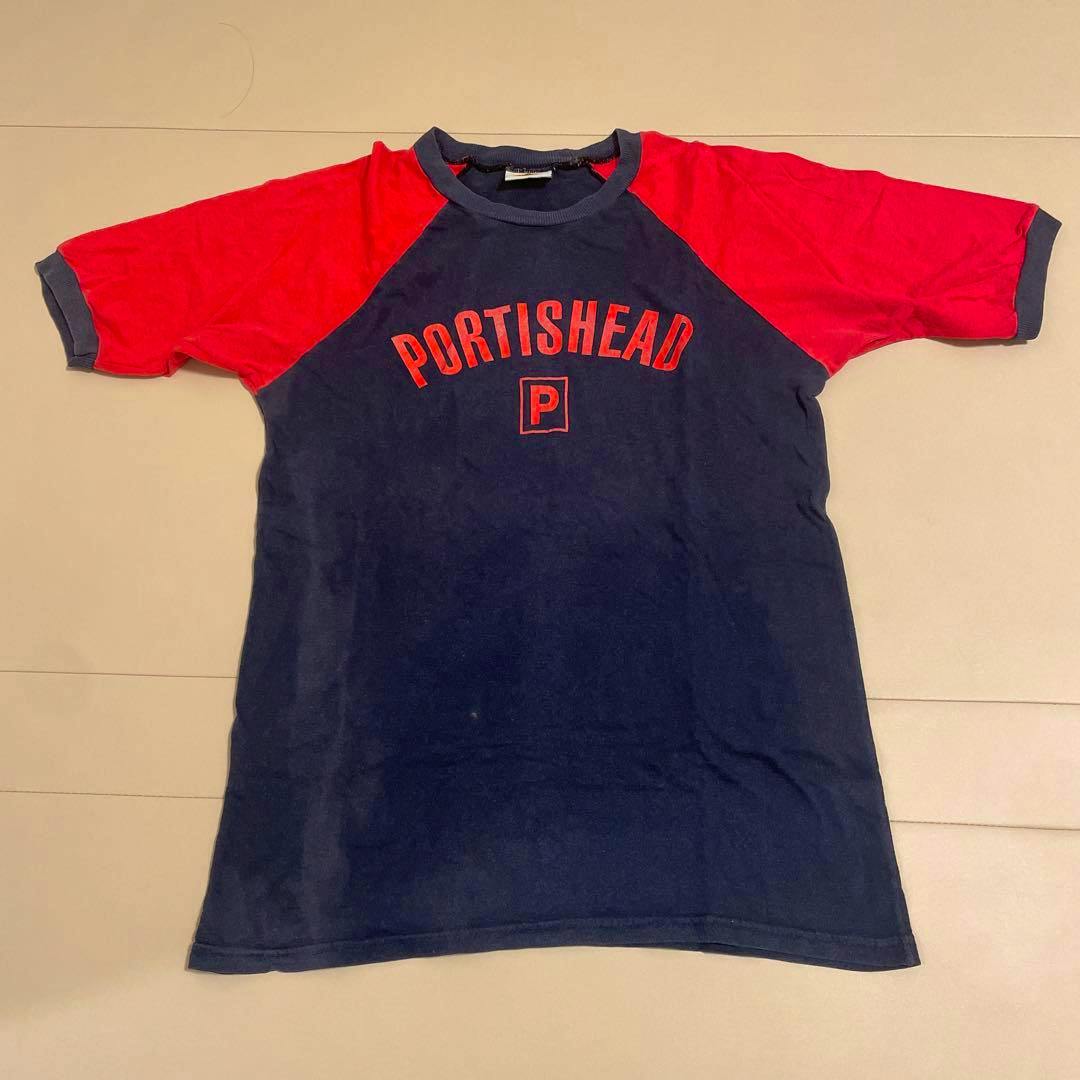 Flat-lay navy and red raglan men's cotton T-shirt with "PORTISHEAD" text on the chest.