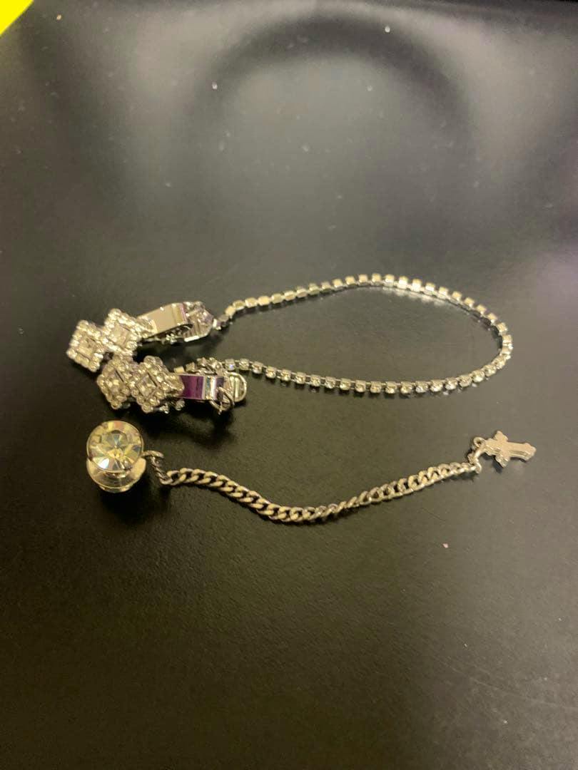 Two silver lapel pin chains on a black surface, one with rhinestone clips and one with a small cross charm.