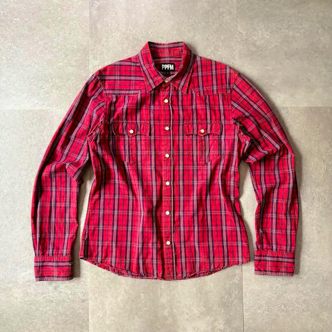 PPFM red check long-sleeve shirt laid flat on a tile floor showing the front with buttons and chest pockets.