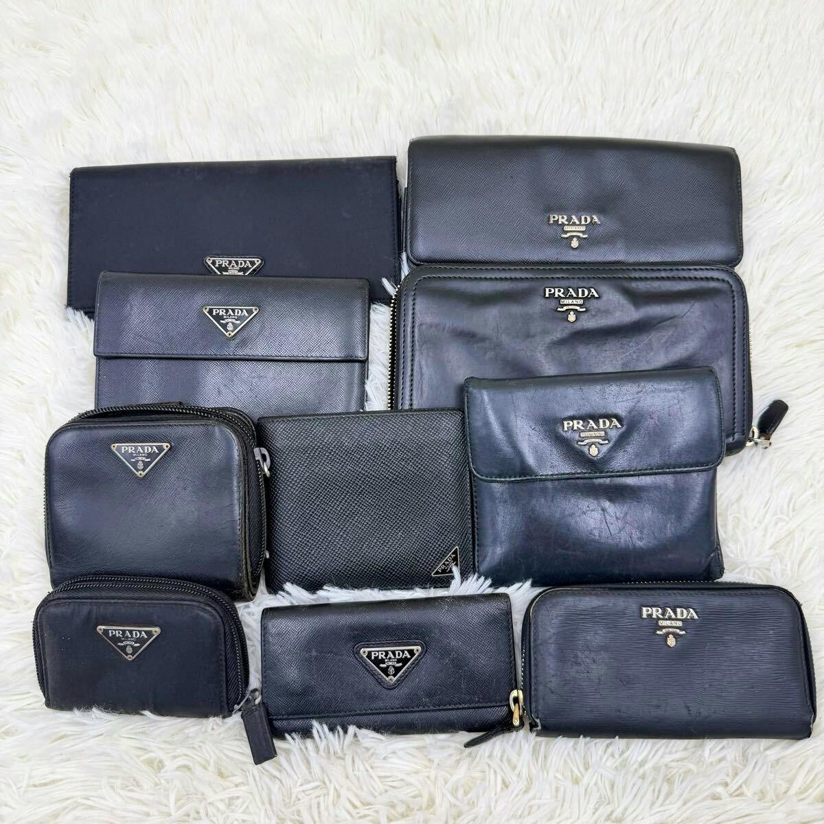 Ten black Prada wallets and small pouches arranged on a white fur background showing triangular and metal Prada logos.