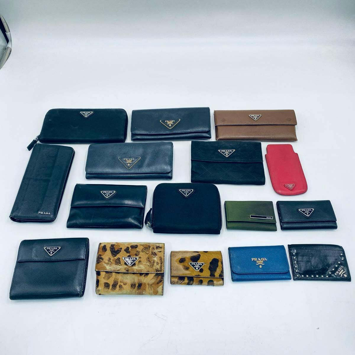 Sixteen Prada wallets and small leather accessories arranged on a white background, showing various styles and colors.