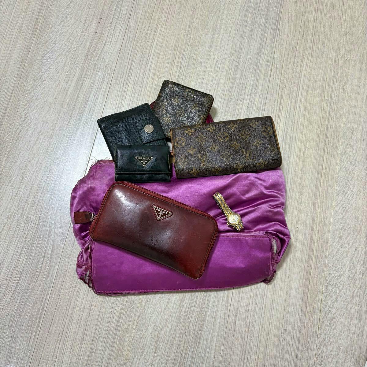 Assorted wallets including a PRADA zip wallet displayed on a purple cloth on a light wood floor.
