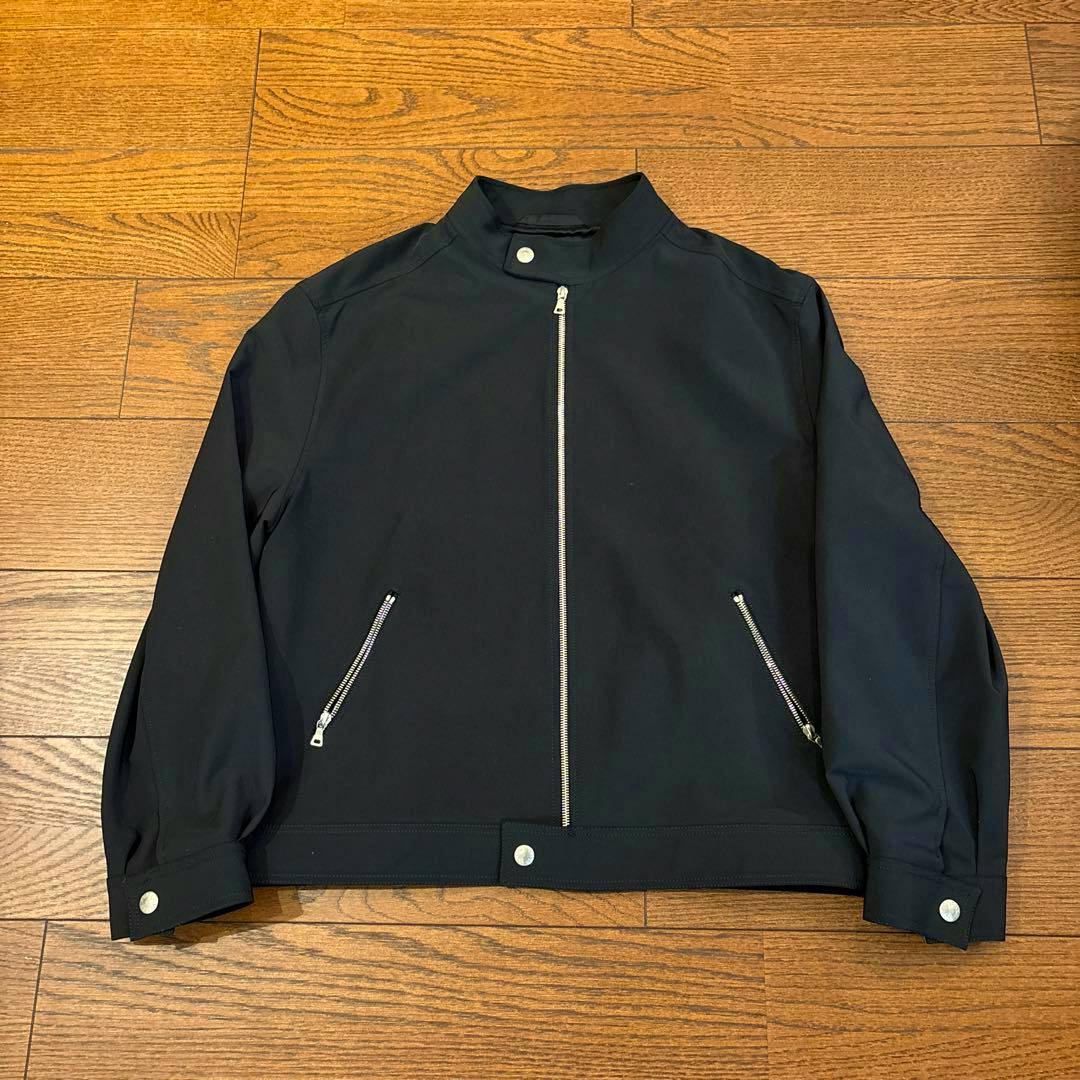 Black PRADA men's nylon blouson jacket laid flat on a wooden floor showing the front zipper and two zippered pockets.