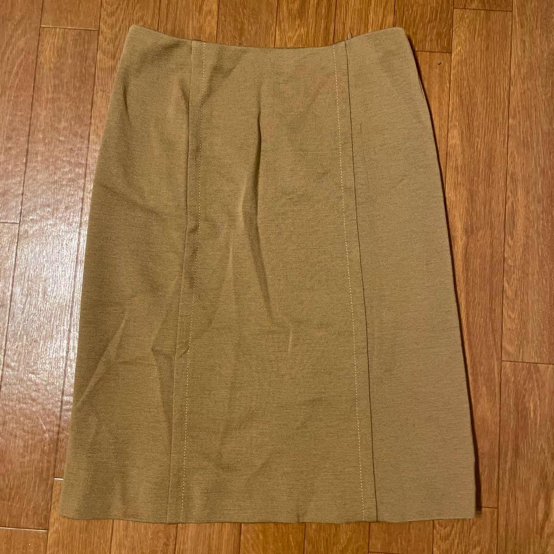 Beige knee-length skirt laid flat on a wooden floor.