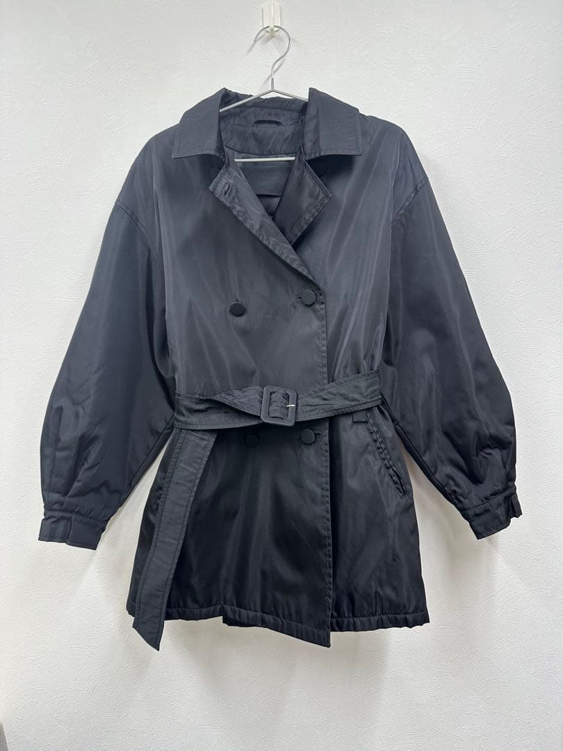 Black Prada double-breasted women's acetate jacket with belt hanging on a hanger against a white wall.